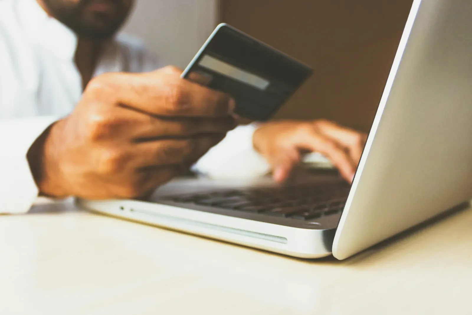Person hält eine Bankkarte in der Hand und tippt auf einer Notebook-Tastatur