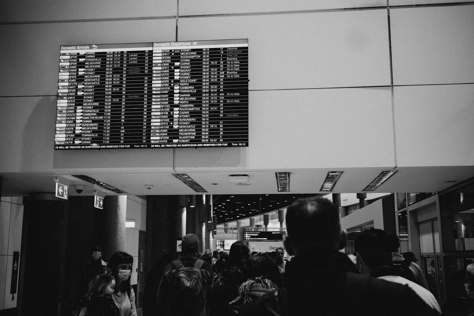 Anzeigetafel mit Abflügen über wartenden Reisenden in einer Flughafenhalle